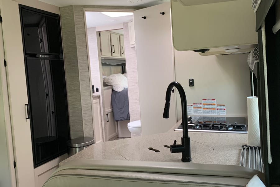 RV rental interior featuring a modern kitchen with black faucet, light dinette seating, and a bright bedroom/bath area.