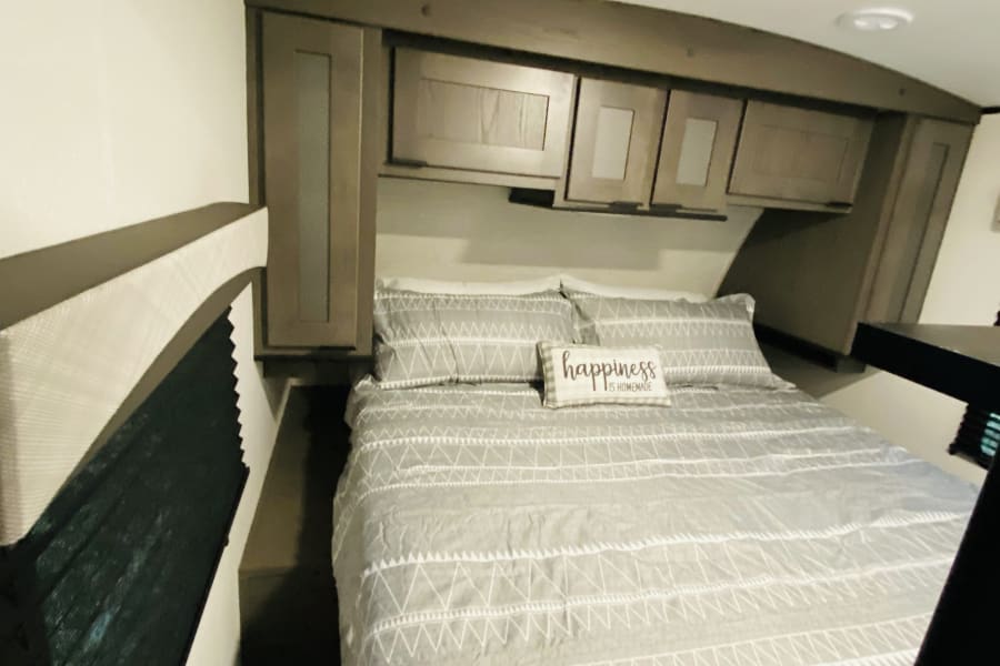 RV rental bedroom with queen bed, overhead cabinets, and window. Cozy interior for your travels.