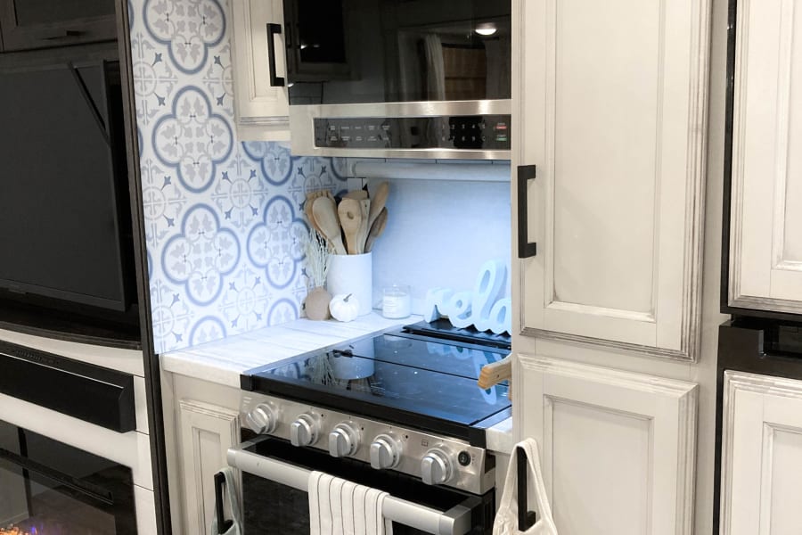 Modern RV rental kitchen: blue tile backsplash, microwave, stove, and fireplace. Your happy place on wheels.