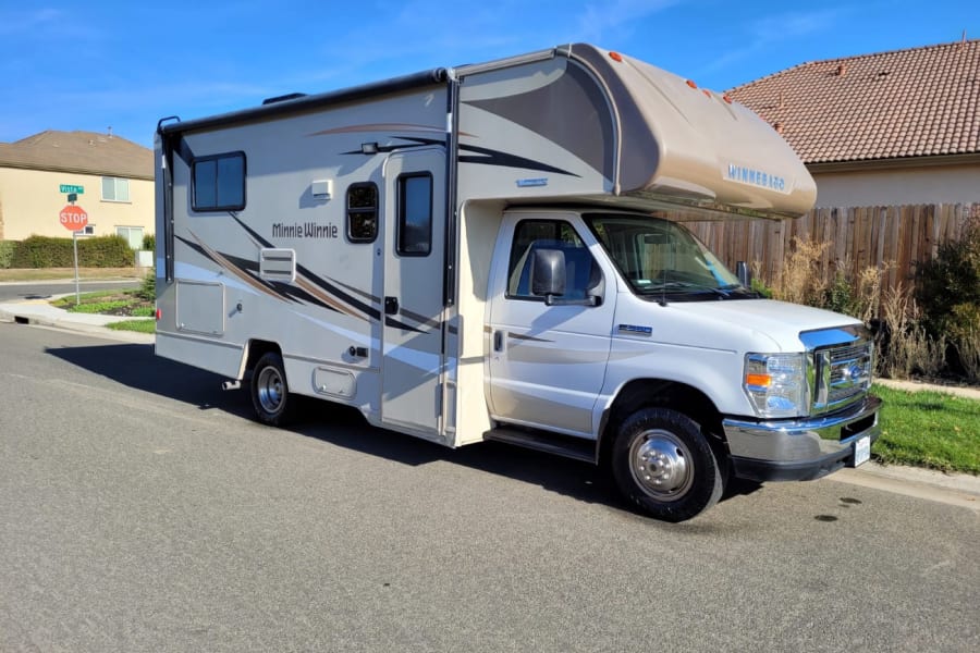 A modern white and beige Winnebago Minnie Winnie RV rental is parked on a sunny residential street.