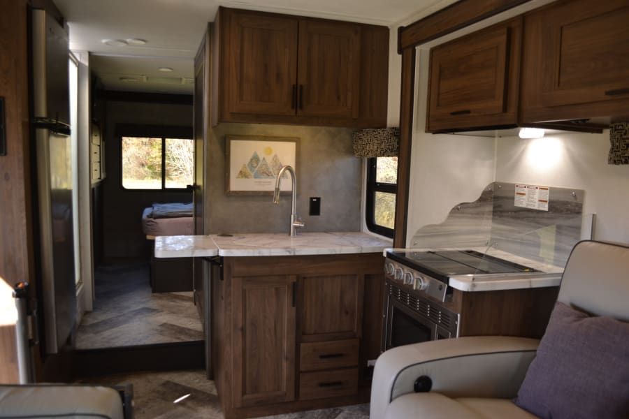 Inviting RV rental interior showcasing a full kitchen, comfortable living space, and a view of the separate bedroom.