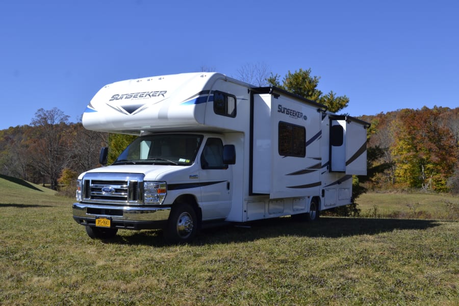 White Sunseeker rv rental, a Class C motorhome, is parked with slide-outs extended in a beautiful autumn landscape.