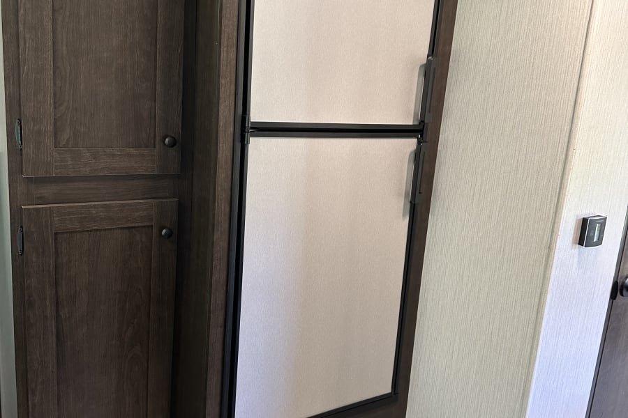 Inside an RV rental: a built-in Dometic refrigerator flanked by dark wood cabinetry with a power panel, designed for compact living.