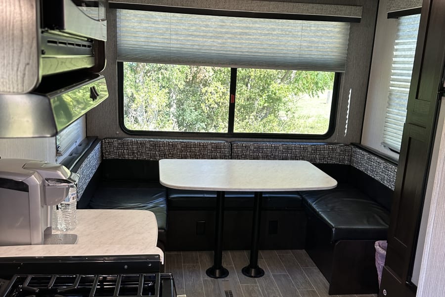 Cozy RV rental interior with kitchen (stove, microwave, coffee maker) and dinette. Large windows offer green views.