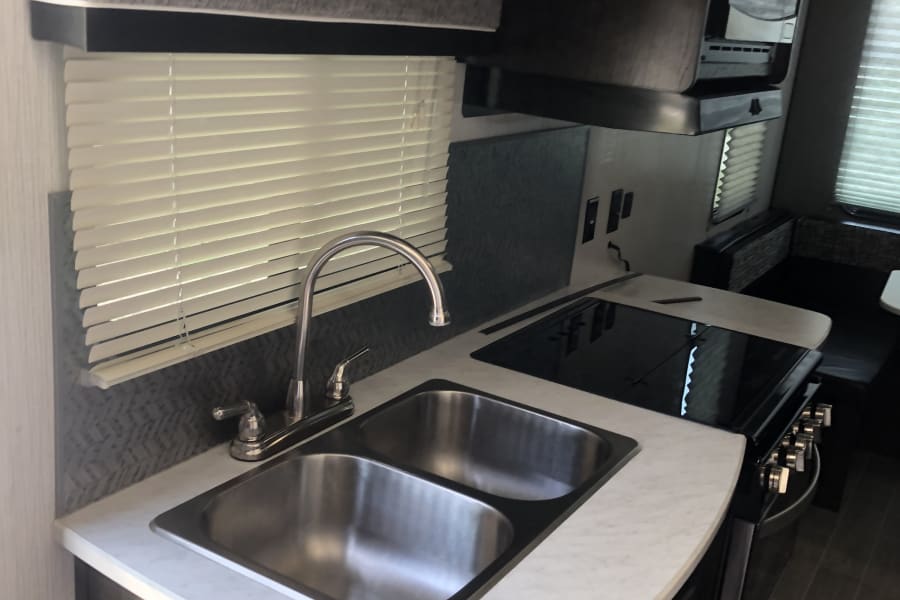 Well-equipped RV rental galley kitchen featuring a double sink, stove, microwave, and storage cabinets.