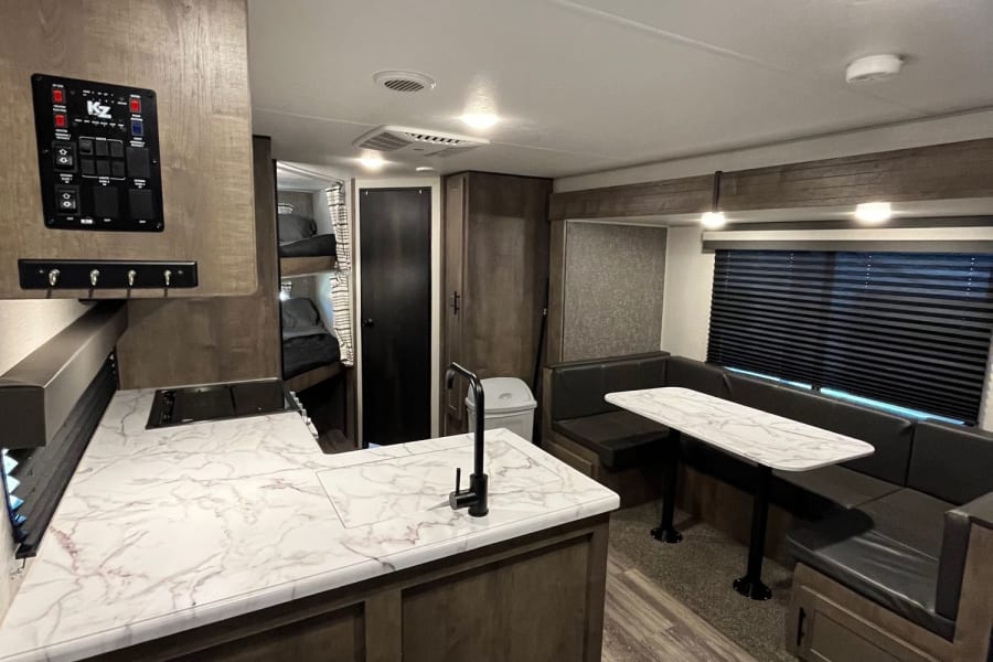 RV rental interior: modern kitchen with marble counters, dining booth, bunk beds, and control panel. Brightly lit living space.