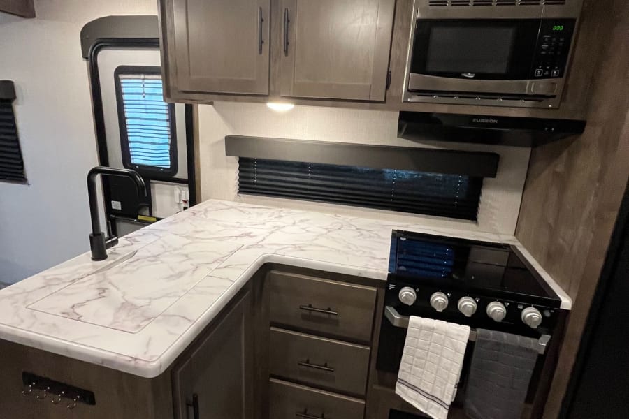 Compact RV rental kitchen features modern dark wood cabinetry, marble-look counters, built-in microwave, and stove.