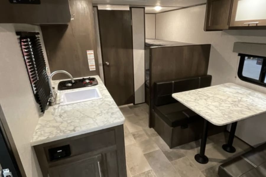 RV rental interior: Kitchen with sink & stove, dinette seating with table, and bunk beds in the rear.
