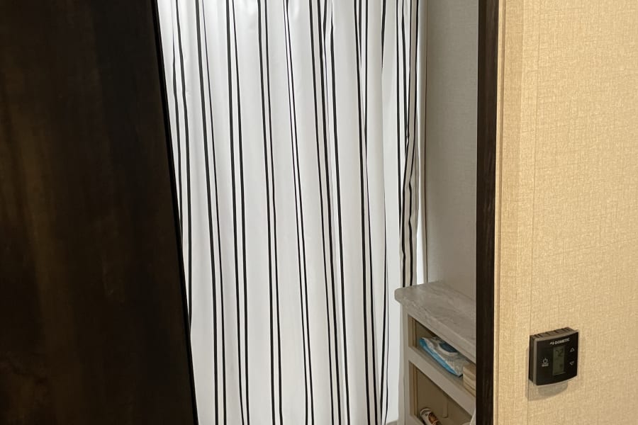 Compact RV rental bathroom featuring a white toilet, striped shower curtain, and vanity with shelving, showcasing travel convenience.