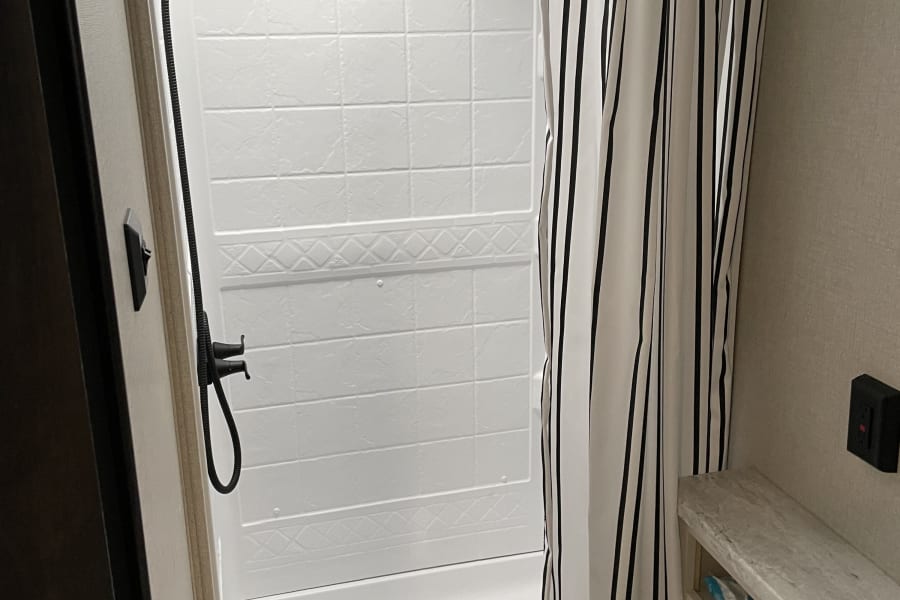 RV rental: Compact bathroom with white shower, black shower head, striped curtain, toilet, and counter.