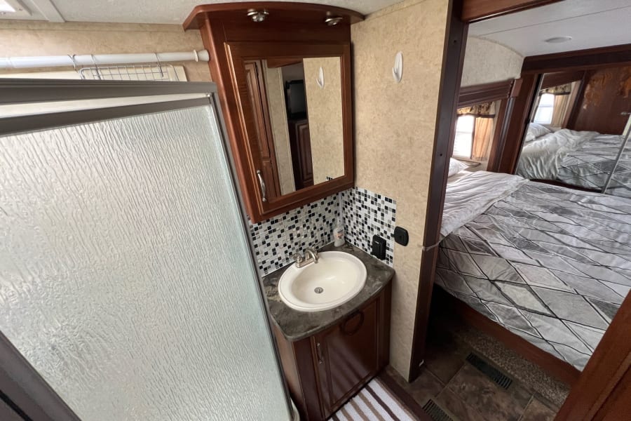 RV rental interior: practical bathroom with shower, sink, and vanity. Bedroom visible beyond. Perfect for travel adventures.