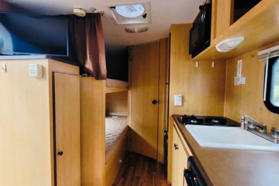 RV rental interior view showcasing a functional kitchen, TV, bunk beds, and light wood cabinetry. Clean & ready for travel.