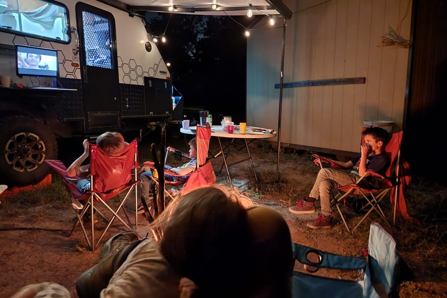 Relaxed family camping under string lights by an RV rental. Kids enjoy outdoor screen time at night.