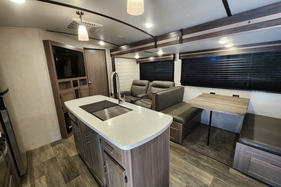 Full interior view of an RV rental with modern kitchen island, comfy recliners, and a dinette.