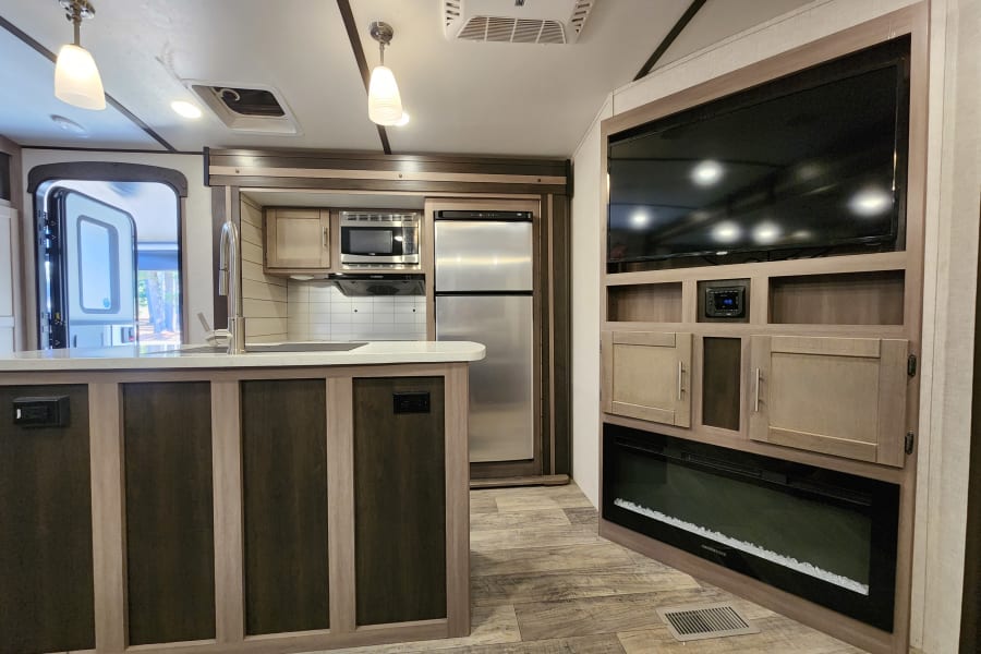 Spacious RV rental interior featuring a modern kitchen island, full kitchen, and living area with TV and fireplace.