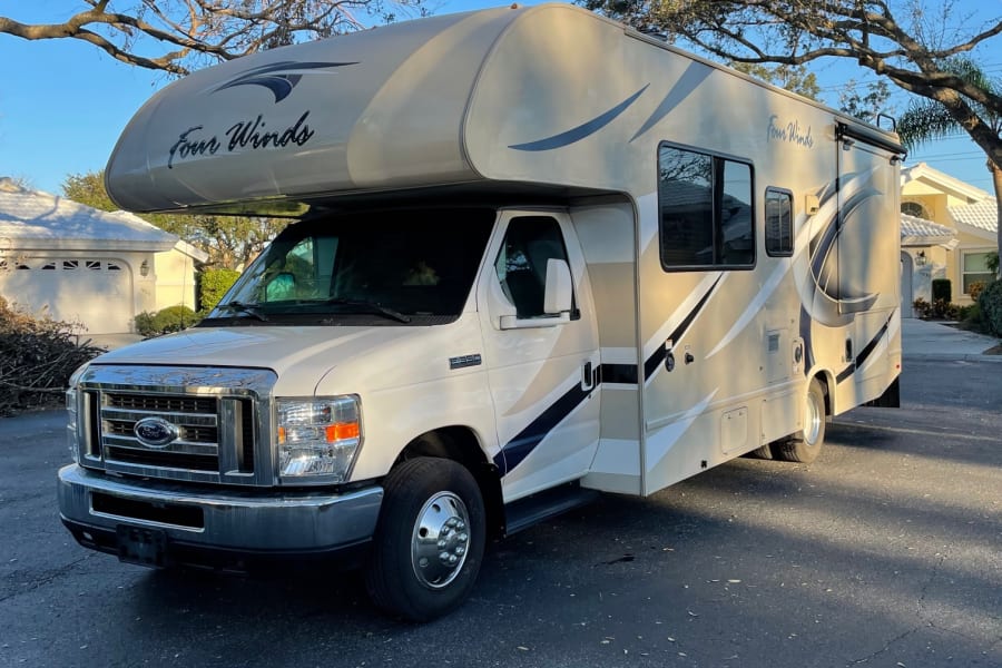 A light-colored Four Winds Class C RV rental, parked on asphalt under a blue sky. Ready for road trips.