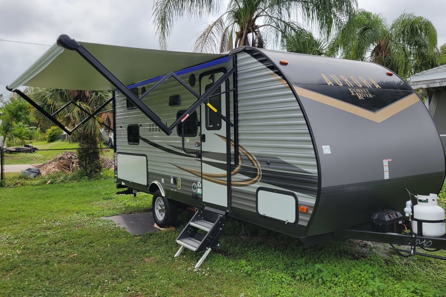 Discover this spacious gray & black travel trailer RV for rent, featuring an extended awning, ready for your next adventure.