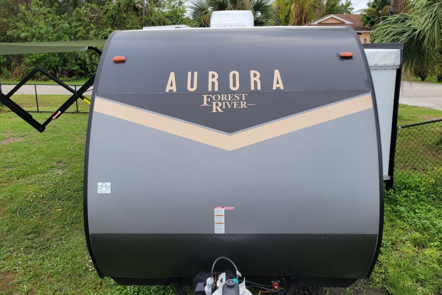 Front of a grey and beige Aurora Forest River travel trailer, perfect for an RV rental. Awning extended.