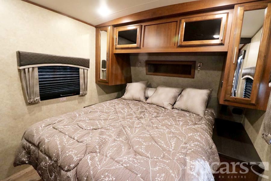Explore a comfortable RV rental bedroom, featuring a cozy bed, ample wood cabinetry, and a window with blinds.