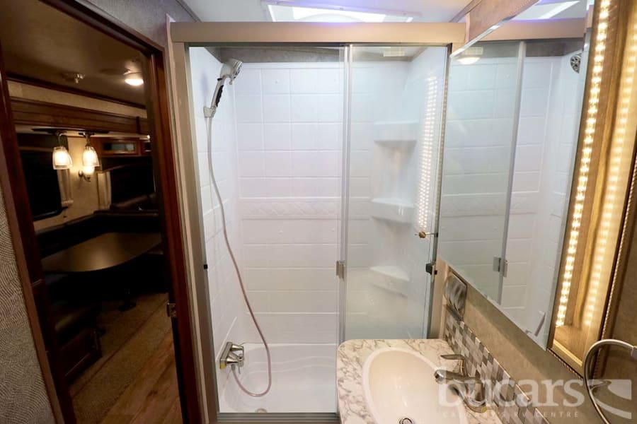Explore this RV rental: a clean bathroom with a walk-in shower, vanity, and a glimpse of the comfortable living area.