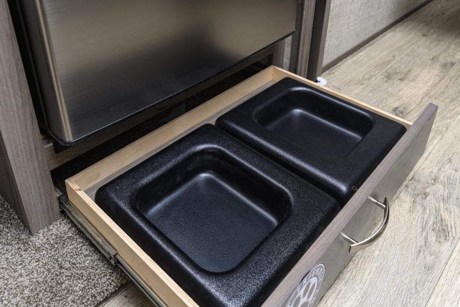 RV rental pet station: Pull-out drawer with integrated pet food/water bowls under an appliance, designed for convenience.