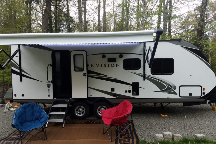 This RV rental is set up for camping with an extended awning, mat, and two chairs. Great for outdoor relaxation.