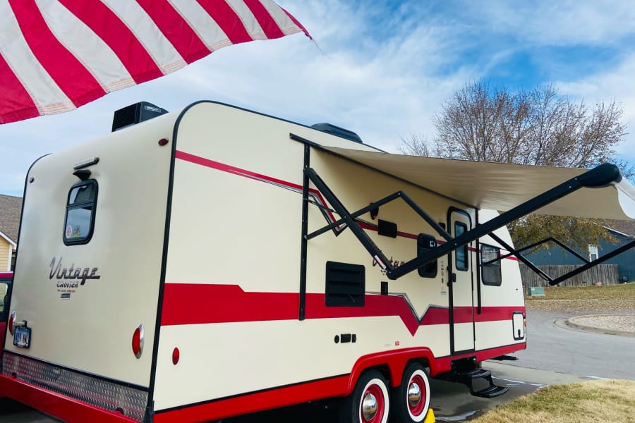 This classic red and beige Vintage Cruiser RV rental is ready for adventure with its awning extended, perfect for camping and road trips.