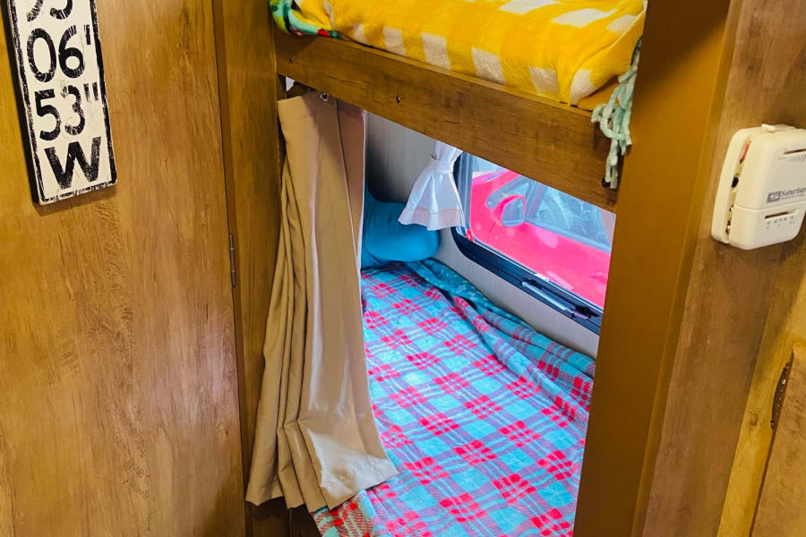 Inside a cozy rv rental, showing bunk beds with bright blankets, a window view, and a thermostat for climate control.