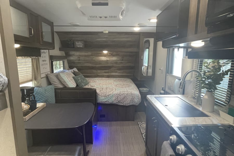 Cozy RV rental interior featuring a full bed, dining booth, and functional kitchen, ideal for your next adventure.