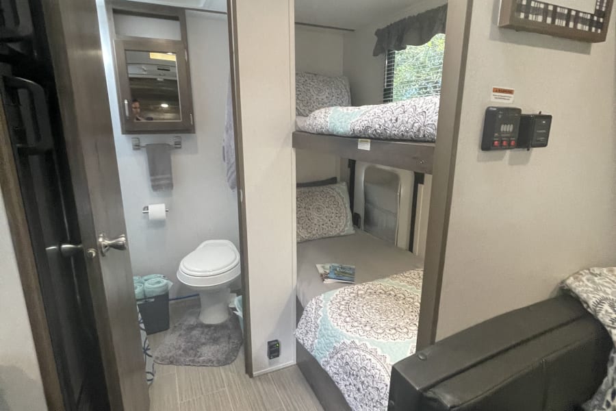 Cozy RV rental interior with bunk beds, compact bathroom, and a seating area. Perfect for family adventures.