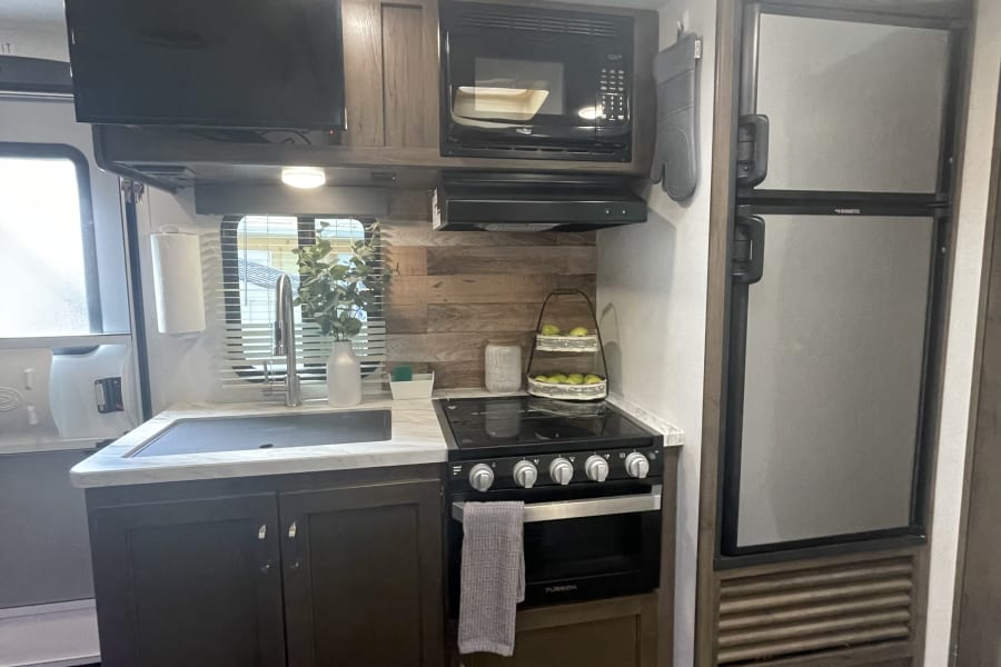 Explore this rv rental's functional kitchen, featuring a TV, microwave, oven, fridge, & sink. Ideal for travel!