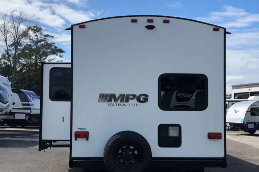 White MPG Ultra-Lite travel trailer RV with a spare tire on the rear, parked outdoors. Great for an rv rental.