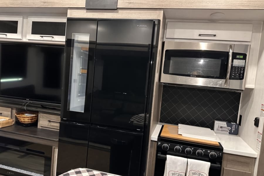 Modern RV rental interior: black Furrion fridge, stainless microwave, range, and TV. A well-equipped kitchen and living space.