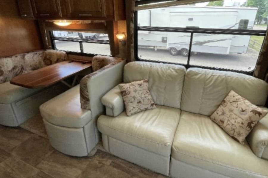 RV rental: inviting interior with light leather sofa, dining booth, and large windows.