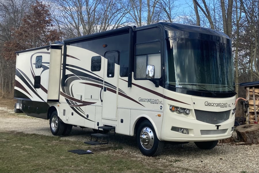 A large white and black Georgetown XL rv rental motorhome with slide-outs extended, parked on a gravel drive with trees.