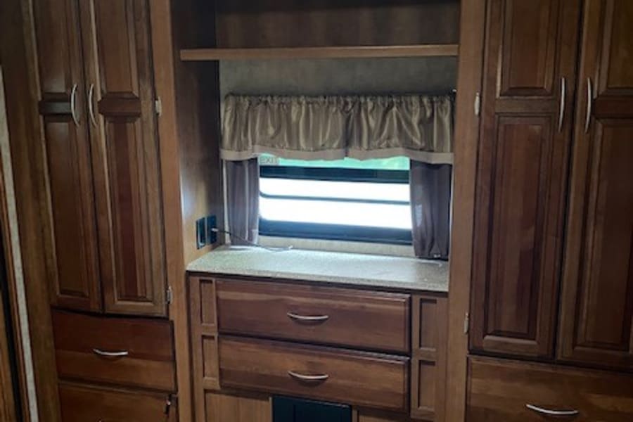 This RV rental interior features rich wood cabinets, drawers, and shelving for ample storage, centered around a window.