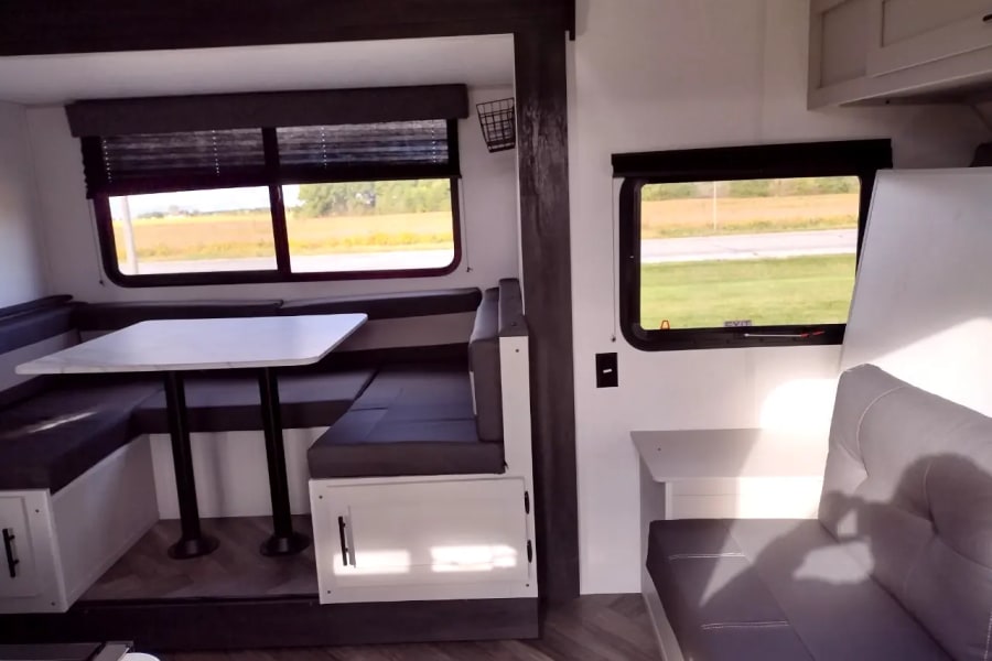 Spacious RV rental interior featuring a dinette, comfortable seating, and large windows with scenic outdoor views. Ideal for travel.
