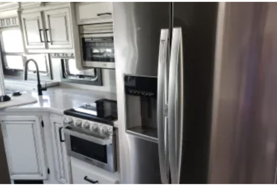 Modern RV rental kitchen interior: stainless steel fridge, stove, and sink with white cabinetry visible.