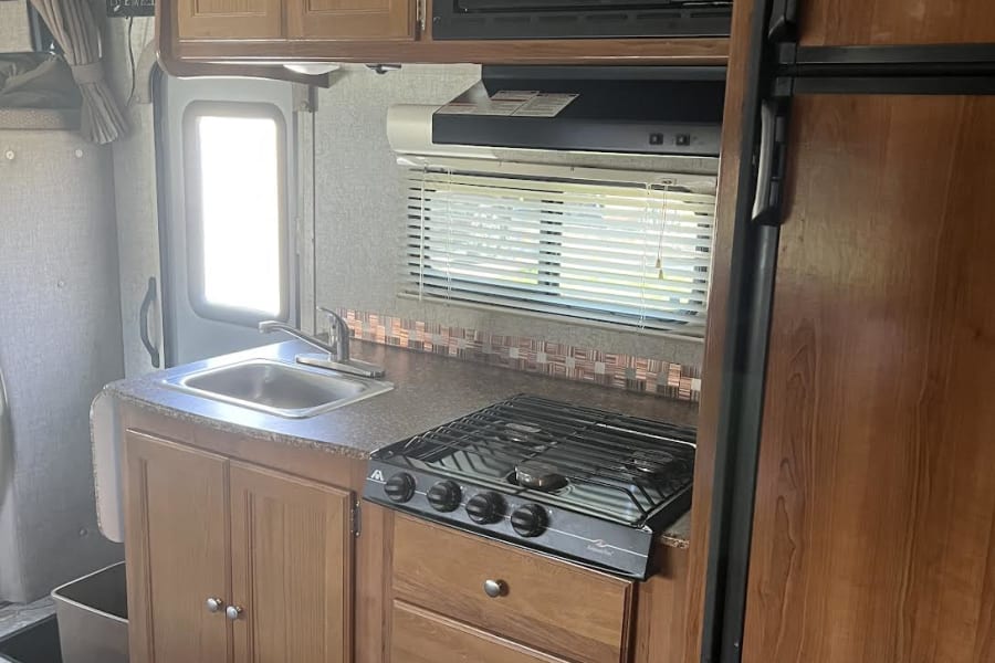RV rental interior: A compact kitchen galley with a microwave, 3-burner stovetop, sink, and wood cabinets.