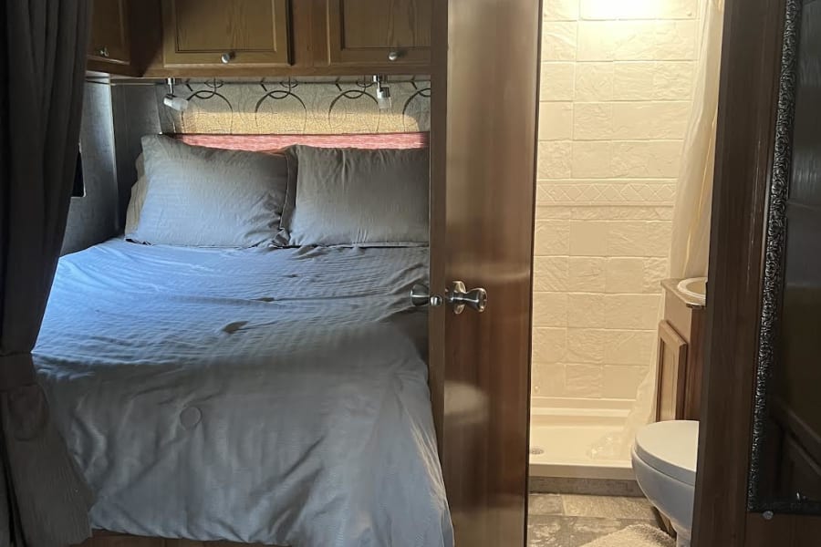 RV rental interior: A cozy bedroom with bed and overhead storage, leading to a compact bathroom with shower and toilet.