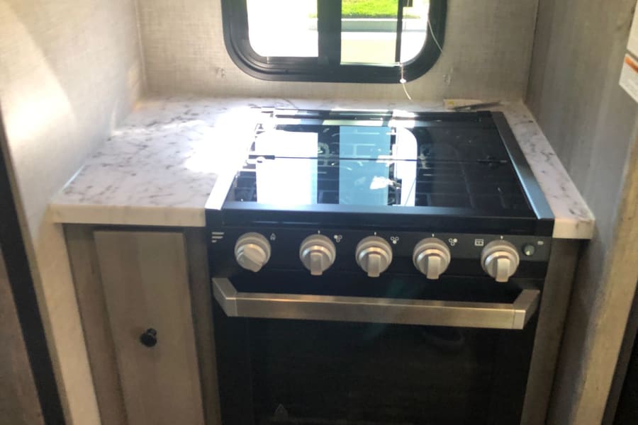 RV rental kitchen shows a Furrion stove/oven, range hood, and marble-look countertop next to a window.