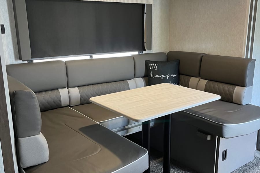 Comfortable RV rental dinette featuring U-shaped gray seating, a light table, and window blind.