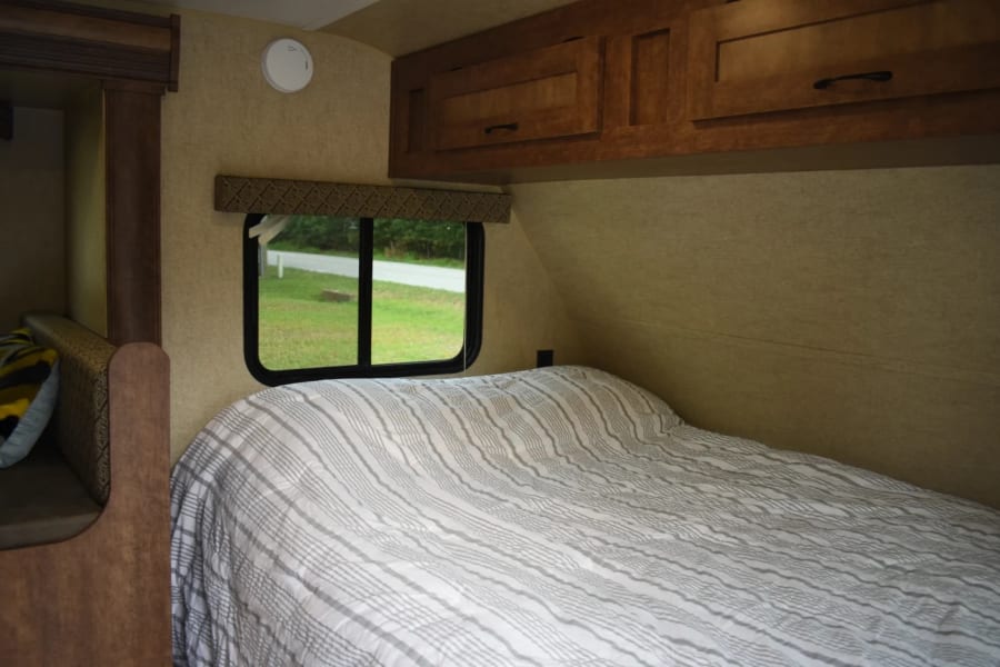 Comfortable RV rental bedroom with striped bedding, window view, and cabinets. Perfect for travel.