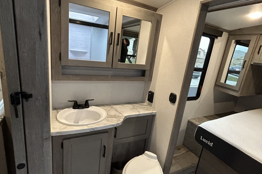 RV rental with compact bathroom: sink, toilet, medicine cabinet, and adjacent Lucid bed for a comfortable stay.
