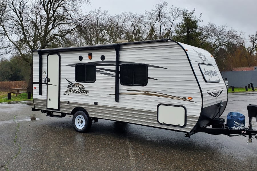 A Jay Flight SLX travel trailer, perfect for your next RV rental, parked on a wet lot under an overcast sky.