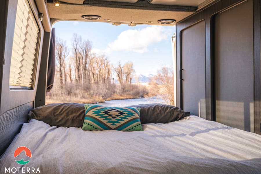 Wake up to stunning views in this comfy RV rental. Camper van bed with scenic river and mountain backdrop.