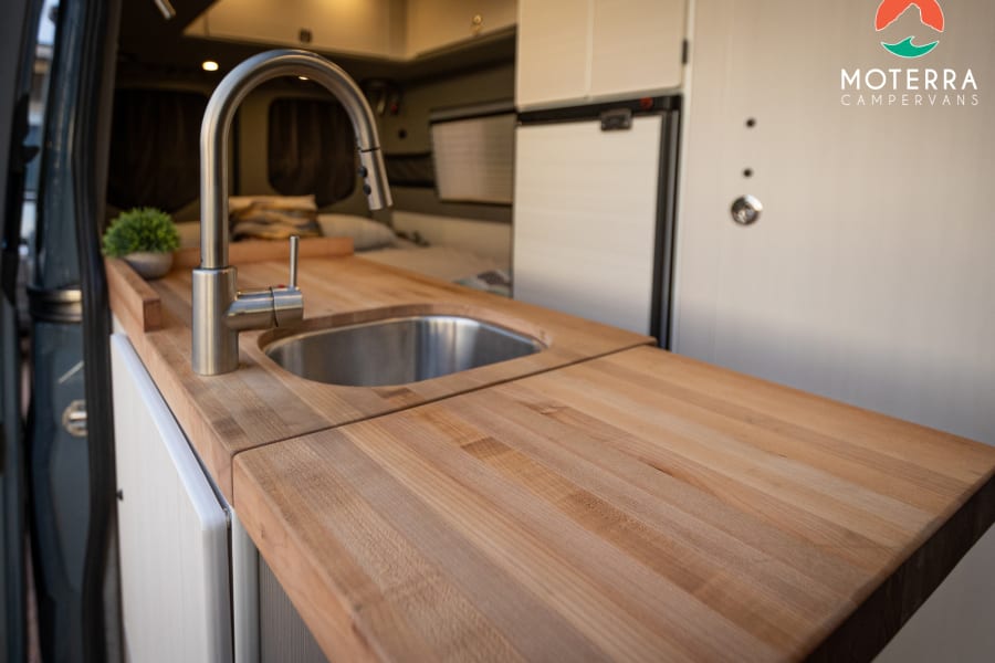 This rv rental features a well-equipped campervan kitchen with a light wood countertop, sink, and modern faucet.