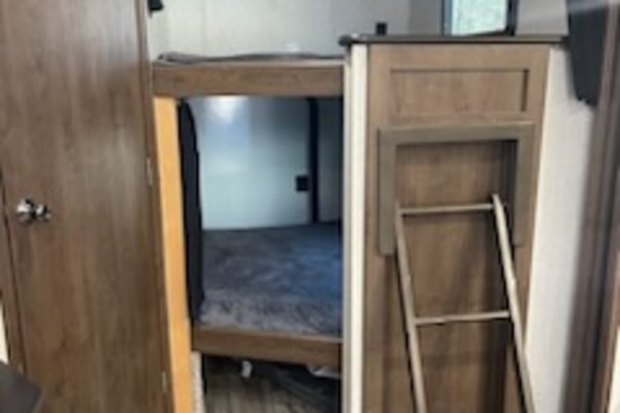 Spacious RV rental bunkhouse with cozy beds and a ladder, perfect for family adventures. Inside this comfortable camper.