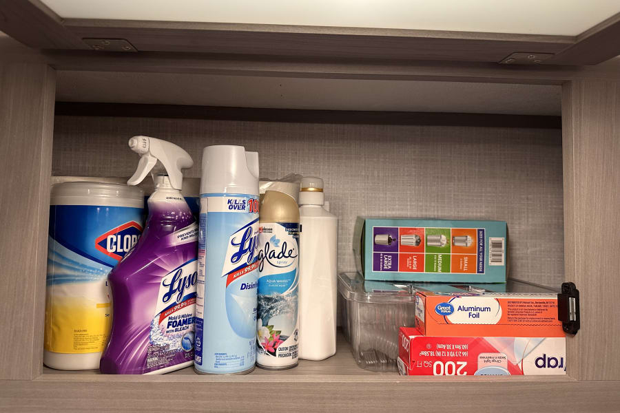 An rv rental cabinet efficiently organized with cleaning supplies like Lysol and Clorox, plus kitchen essentials like foil and wrap.