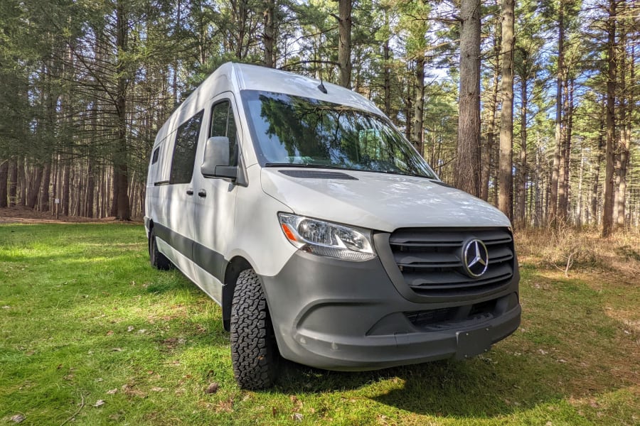 White Mercedes Sprinter camper van, an ideal RV rental for forest camping and nature adventures. Parked on grass.